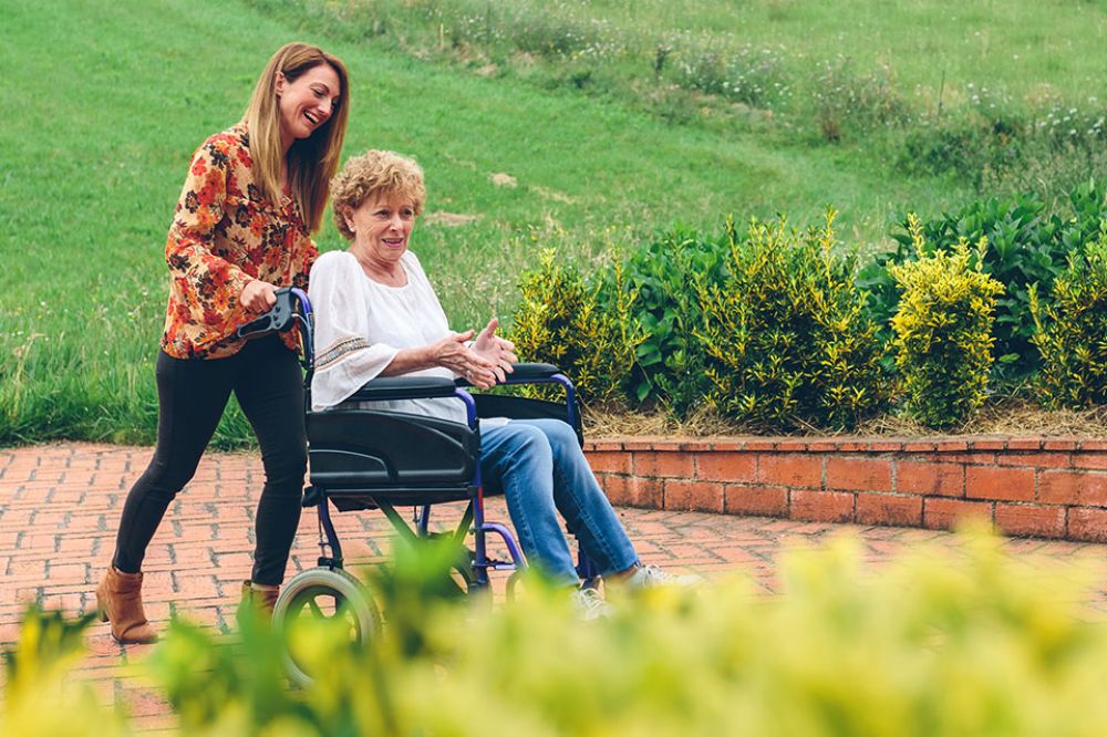 Foto: Pflegerin schiebt Frau im Rollstuhl